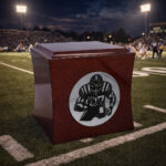 Wooden cremation urn featuring an engraved American football player, placed on a football field under stadium lights at night.