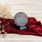 Mini urna decorativa esposta su tessuto rosso con accenti floreali