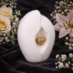 Ceramic cremation urn with gold heart on dark background with flowers