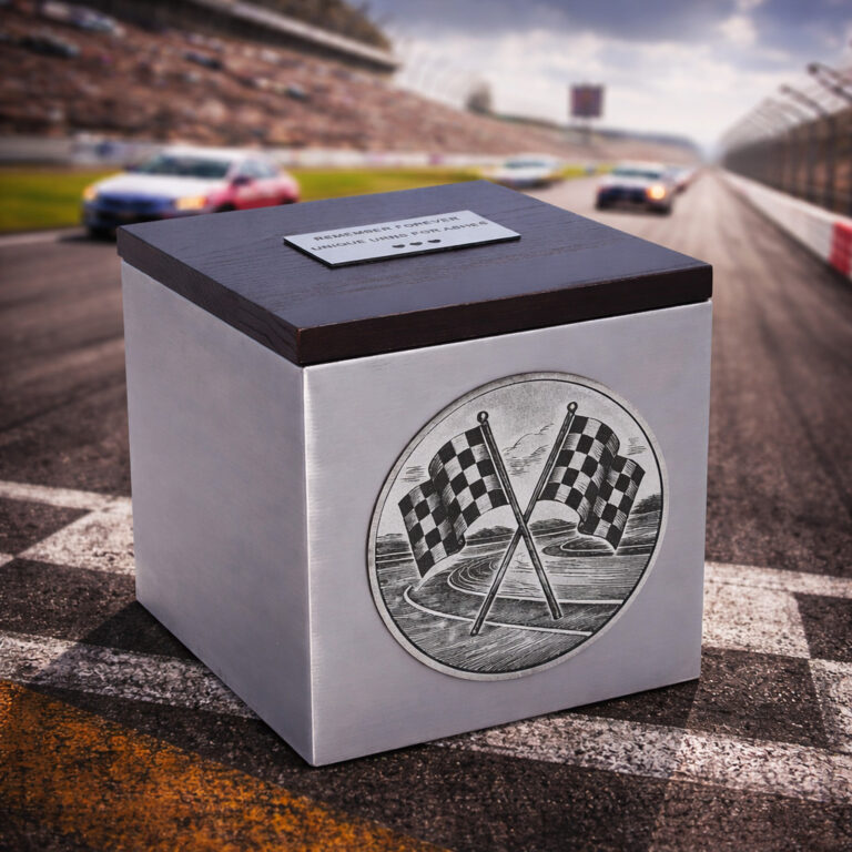 Stainless steel cremation urn with wooden lid and engraved racing flags design, placed on a racetrack with cars in motion.