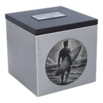 Surfer-Gedenkurne, gebürsteter Edelstahlbehälter mit dunklem Holzdeckel und eingraviertem Surfer mit Surfbrett, schräge Ansicht.