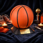 Basketball-shaped cremation urn displayed on a stand, surrounded by sports memorabilia and candles.