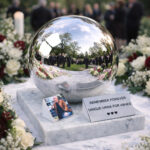 Reflective sphere cremation urn with photo display at an outdoor funeral ceremony with flowers.