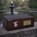 Wooden cremation urn with photo frame placed outdoors near a garden fountain.