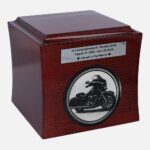 Wooden cremation urn with engraved Harley-Davidson motorcycle and memorial plaque, front view.