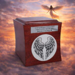 Wooden cremation urn for ashes with angel wings engraving against a heavenly sky background.